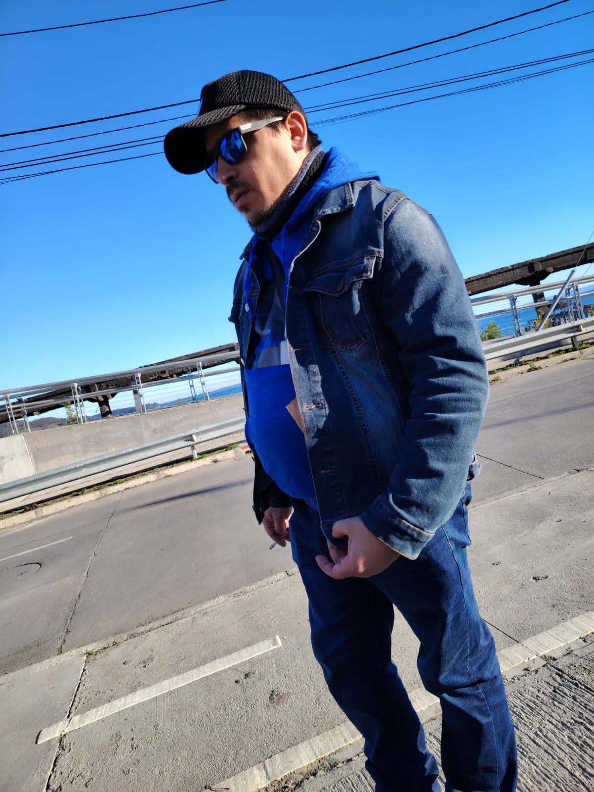 El hombre, presumiblemente en la treintena, presenta una complexión física robusta, con hombros anchos y una estructura corporal que denota cierta musculatura, aunque no excesiva. Su piel, de tono claro, exhibe un ligero bronceado que sugiere exposición regular al sol. Se aprecian sutiles arrugas alrededor de los ojos y en la frente, indicativas de la edad y expresión. La barba incipiente, de color negro intenso, cubre su mandíbula y labio superior, añadiendo un toque de rudeza a su apariencia.